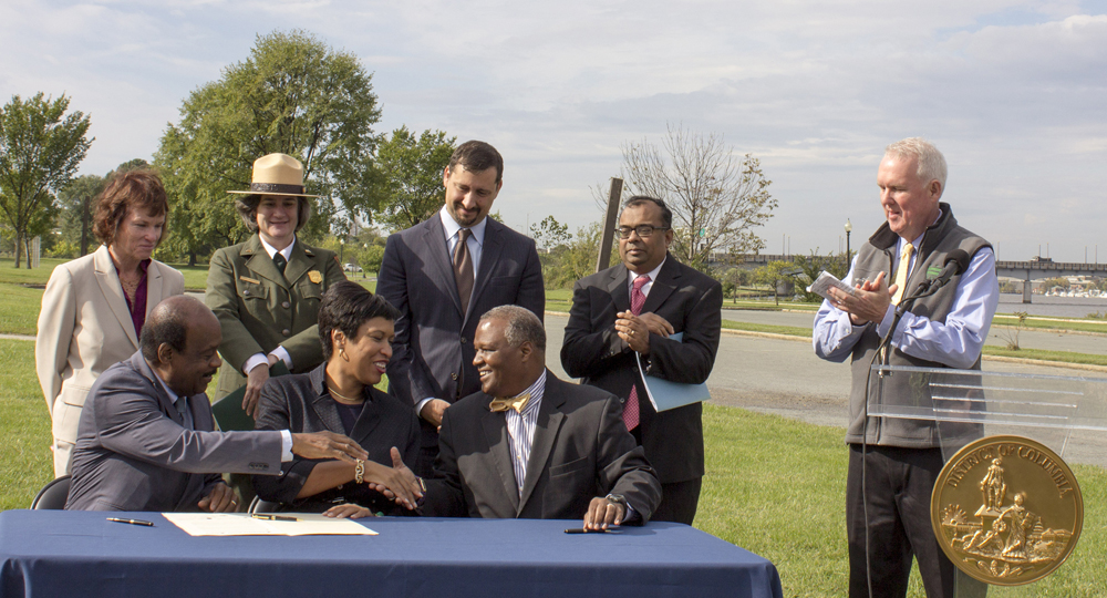 Officials at table shake hands after signing the Anacostia Accord. 